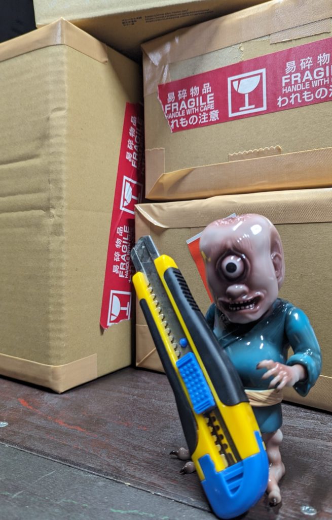 梱包作業をする一つ目小僧のフィギュアの写真。カッターを持っている。