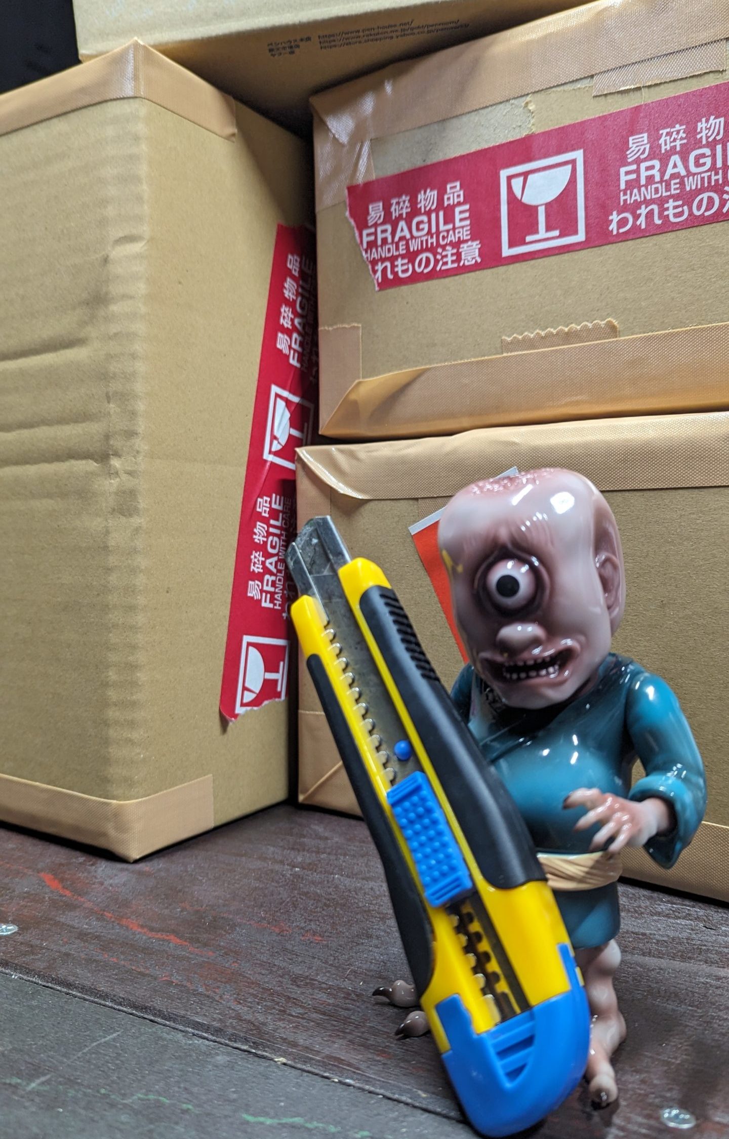梱包作業をする一つ目小僧のフィギュアの写真。カッターを持っている。